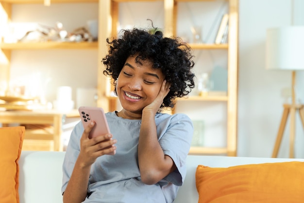 Feliz jovem negra afro-americana segurando o celular rindo sentindo alegria recebendo mensagem móvel Garota muito feliz rindo alto sentado no sofá assistindo vídeo engraçado lendo notícias