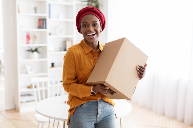 Feliz jovem negra segurando a caixa de entrega em casa