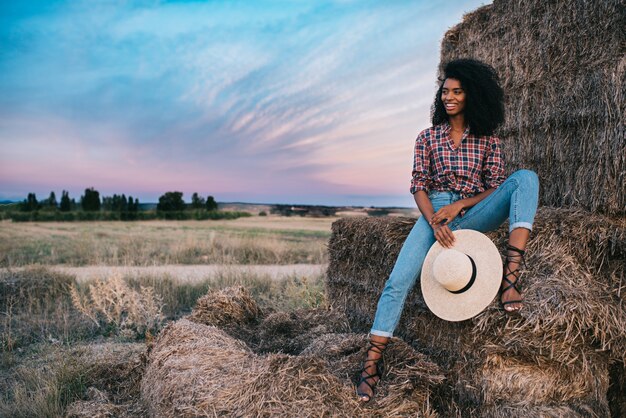 Feliz jovem negra sentada sobre uma pilha de feno