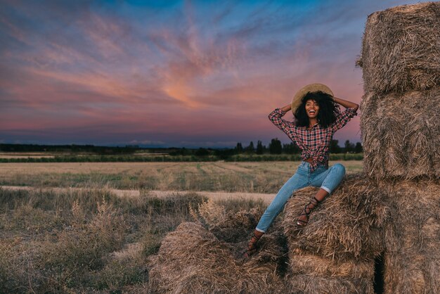 Feliz jovem negra sentada sobre uma pilha de feno