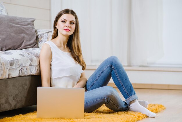 Feliz jovem ou estudante com laptop sentado no chão em casa