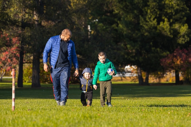 Feliz jovem pai brincando com seu bebê e filho em um parque em um gramado verde