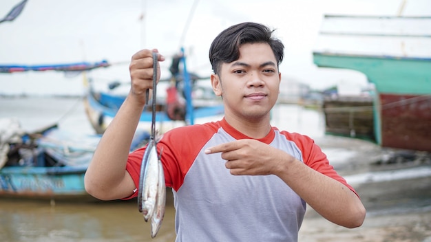 Feliz jovem pescador na praia segurando sua pescaria e shows na frente de seu barco