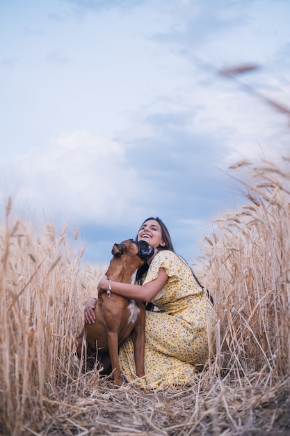 Feliz joven abrazando a su perro mientras disfruta del día juntos al aire libre en un campo de trigo.