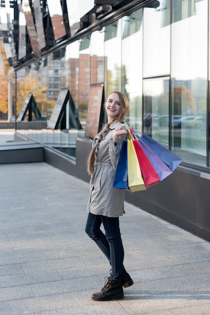 Feliz joven adicto a las compras con bolsas de colores cerca del centro comercial, caminando en la calle.