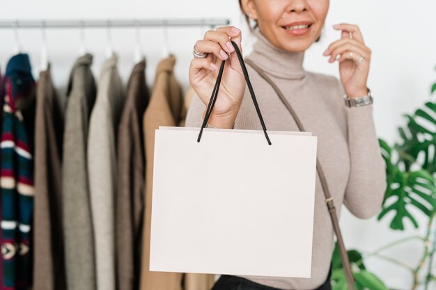 Feliz joven adicto a las compras en ropa casual con bolsa de papel blanca