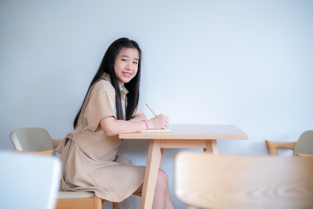 Foto feliz de joven adolescente asiática estudiante universitaria tomando notas escritas en el cuaderno educación en línea concepto de aprendizaje electrónico personas independientes empresarias