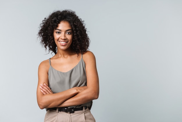 Feliz joven africana vestida casualmente que se encuentran aisladas, con los brazos cruzados