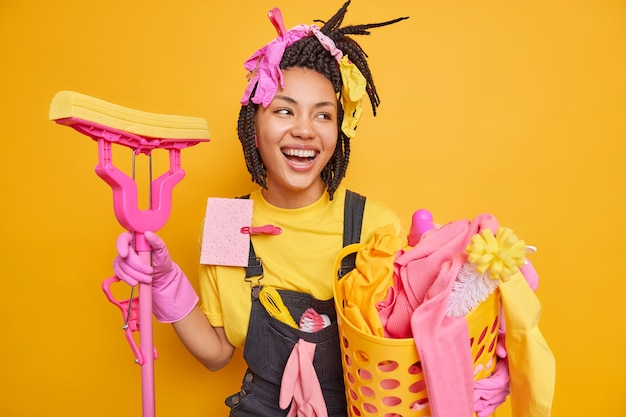 Feliz joven afroamericana ama de casa sostiene la fregona y la palangana de lavandería se ve con alegría