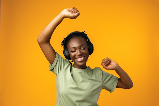 Feliz joven afroamericana escuchando música en auriculares con fondo amarillo