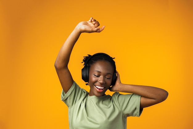 Feliz joven afroamericana escuchando música en auriculares con fondo amarillo