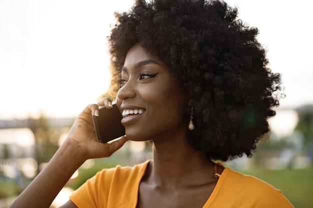 Feliz joven afroamericana hablando con celular en la ciudad