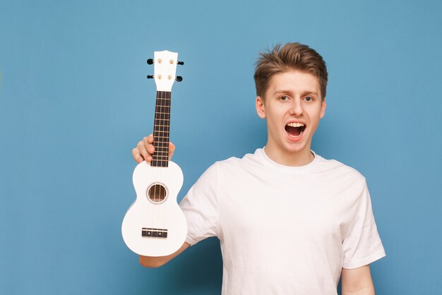 Feliz joven aislado en azul con ukelele en mano