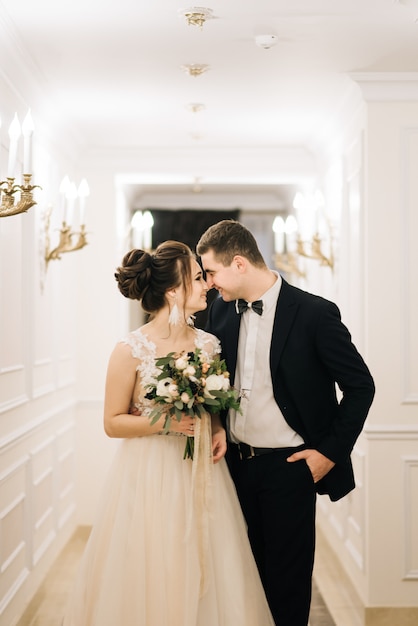 Feliz joven y amorosa novia y el novio caminan por el pasillo de un hotel de lujo. Día de la boda