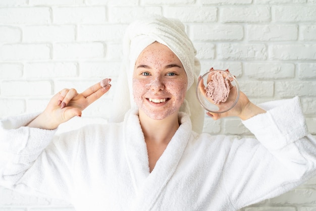 Feliz joven aplicando exfoliante facial en la cara divirtiéndose