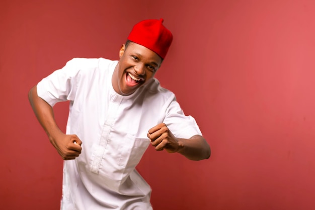 Feliz joven apuesto hombre africano bailando con un sombrero rojo y una camisa blanca