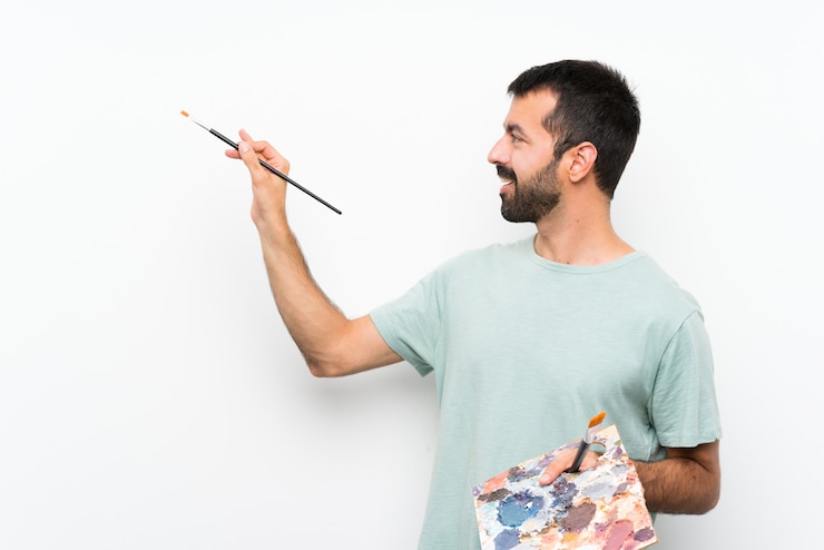 Foto feliz joven artista hombre sosteniendo una paleta sobre pared aislada