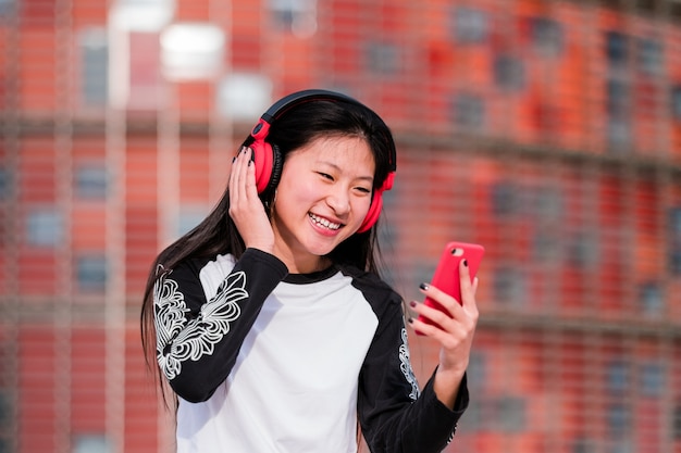 Feliz joven asiática con auriculares con smartphone en las calles de la ciudad