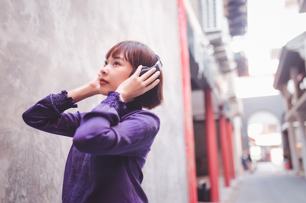 Feliz joven asiática escuchando música con auriculares en la calle.