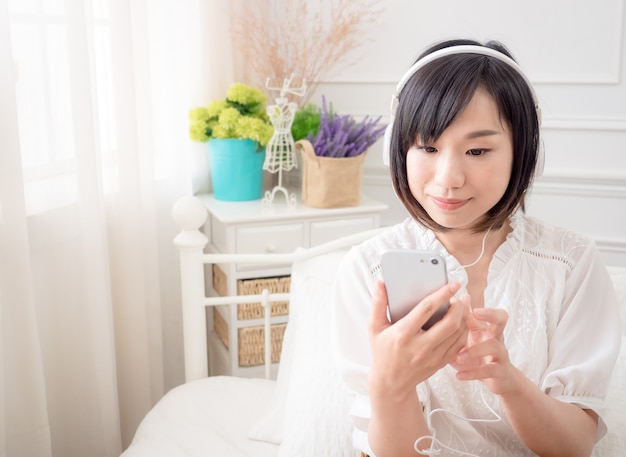 Feliz joven asiática escuchando música en la cama