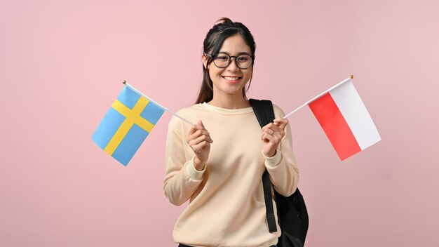 Feliz joven asiática mostrando la bandera de Polonia y Suecia sobre fondo rosa aislado