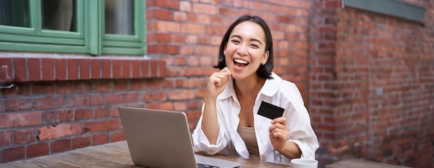 Feliz joven asiática sentada cerca de una computadora portátil con tarjeta de crédito pagando facturas comprando en línea