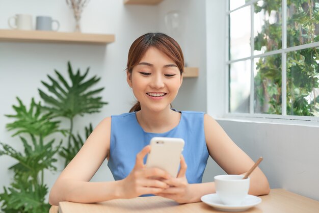 Feliz joven asiática con smartphone y tomando café en la mesa