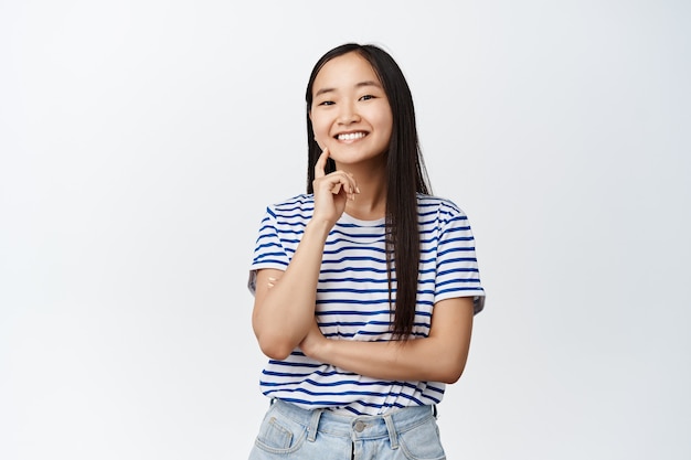 Feliz joven asiática con sonrisa blanca saludable, mirando confiado, de pie en camiseta en blanco