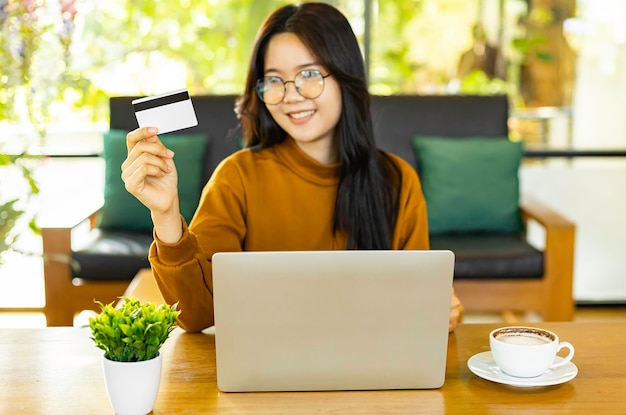 Feliz joven asiática con tarjeta de crédito y usando una computadora portátil para pago electrónico en una tienda remota en línea de Internet