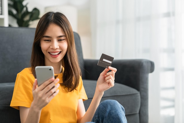 Foto feliz joven asiática con tarjeta de crédito y usando un teléfono inteligente para comprar en línea con pago en banca por internet