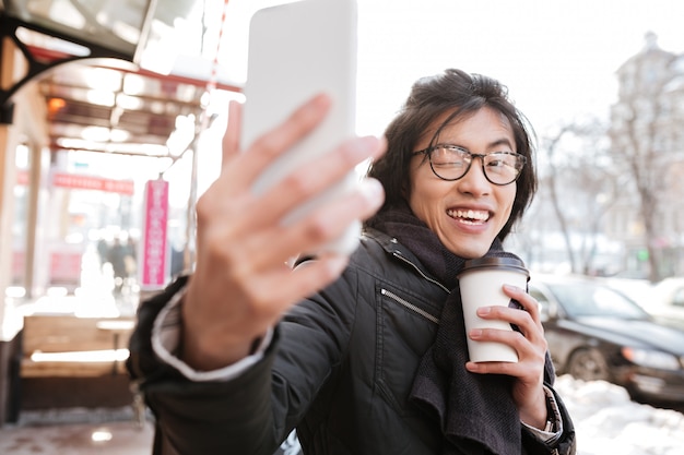 Feliz joven asiática tomando café y hacer selfie.