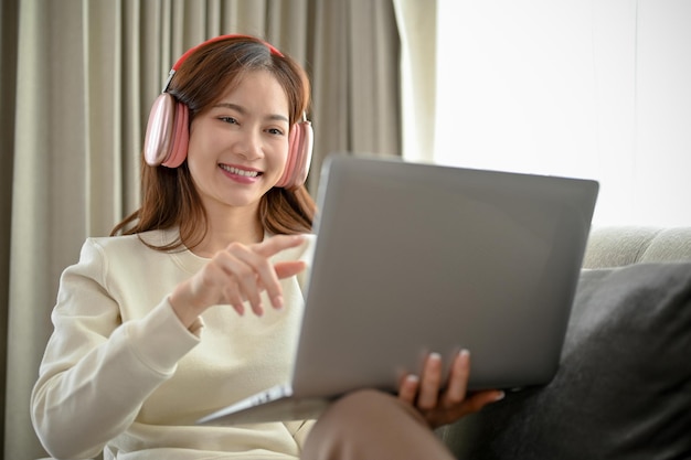 Feliz joven asiática usando audífonos y viendo películas en una computadora portátil