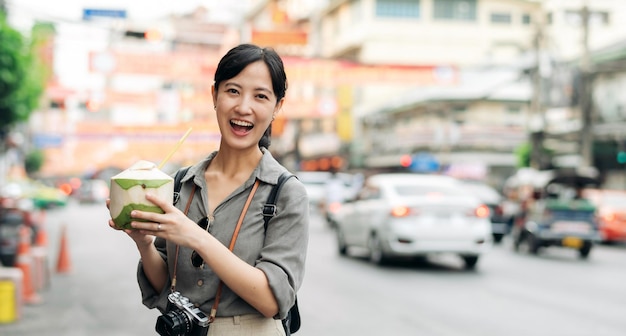 Feliz joven asiática viajera con mochila bebiendo un jugo de coco en el mercado de comida callejera de China Town en Bangkok Tailandia Viajero revisando calles laterales