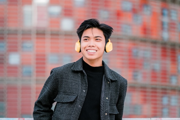 Feliz joven asiático con auriculares en las calles de la ciudad