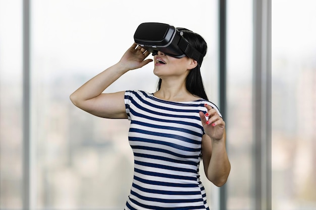 Feliz joven asombrada está teniendo experiencia de realidad virtual fondo de ventanas borrosas