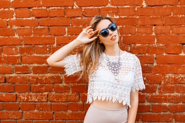 Feliz joven atractiva mujer hipster en gafas de sol en una blusa de encaje blanco