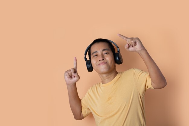 Feliz joven en auriculares escuchando música y bailando sobre fondo naranja studio. Escuchando música.