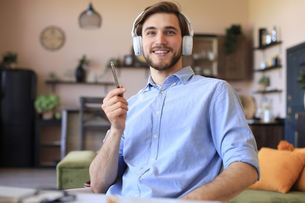 Feliz joven en auriculares trabajando desde casa durante el autoaislamiento.