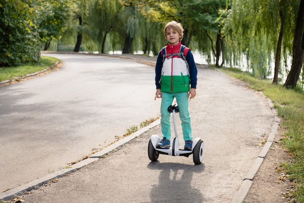 Foto feliz joven balanceo en hoverboard eléctrico en el soleado parque de otoño