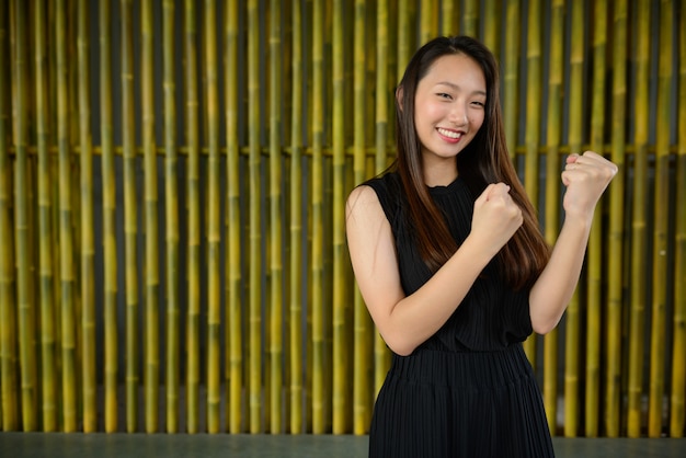 Feliz joven bella empresaria asiática contra la valla de bambú