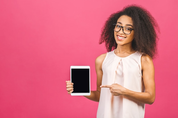 Feliz joven y bella mujer afroamericana mostrando tablet PC en blanco sobre rosa. Dedo señalador.