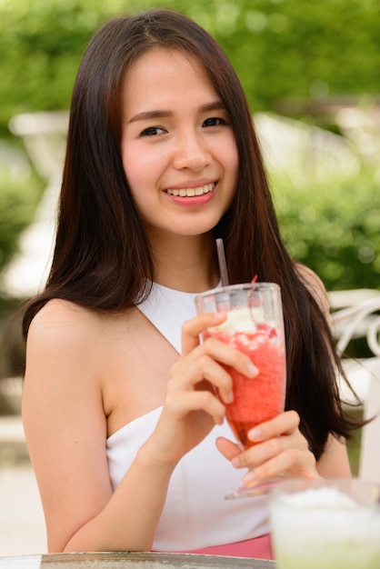 Feliz joven bella mujer asiática con batido en la cafetería al aire libre