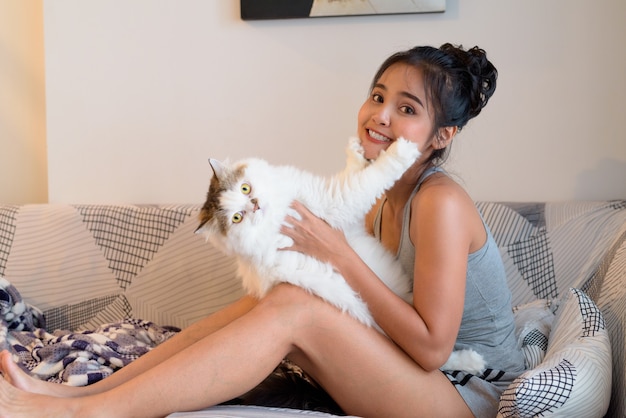 Feliz joven bella mujer asiática jugando con gato persa en la sala de estar en casa