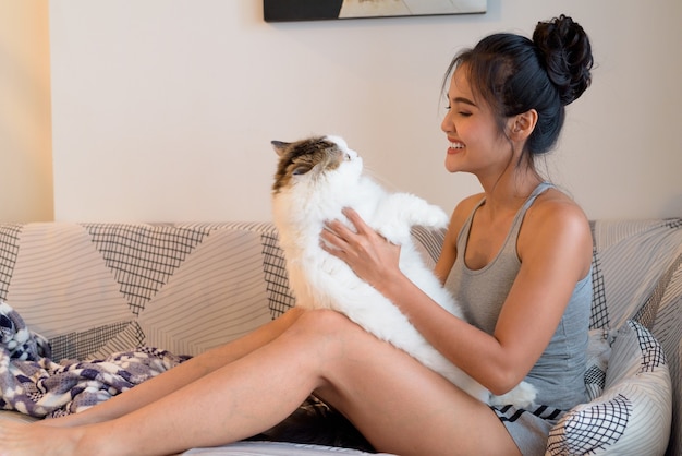 Feliz joven bella mujer asiática jugando con gato persa en el sofá