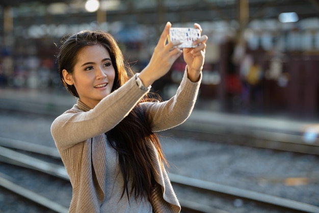 Feliz joven bella mujer asiática tomando selfie en la estación de tren