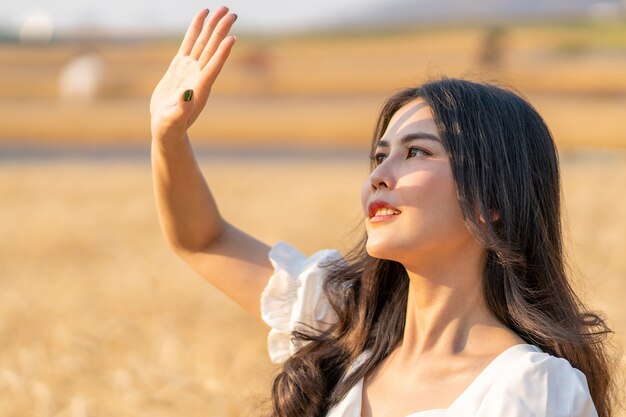 Feliz joven y bella mujer de pie en un campo de cebada levantando su mano para bloquear el sol vespertino