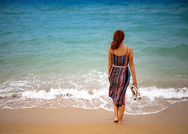 Feliz joven boho mujer caminando y divirtiéndose en las olas del mar en un día cálido y soleado en una isla tropical