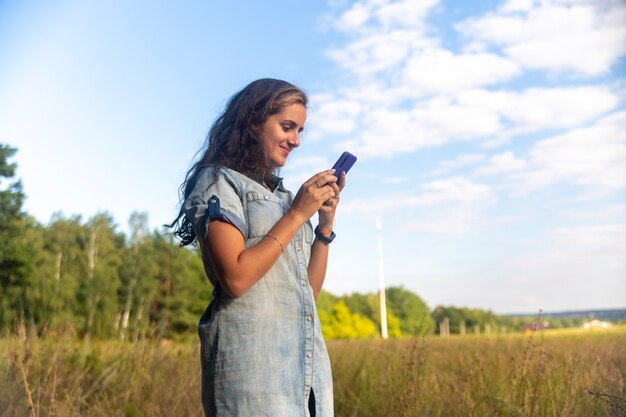 Feliz joven busca en el teléfono inteligente en el fondo de la naturaleza en un día soleado