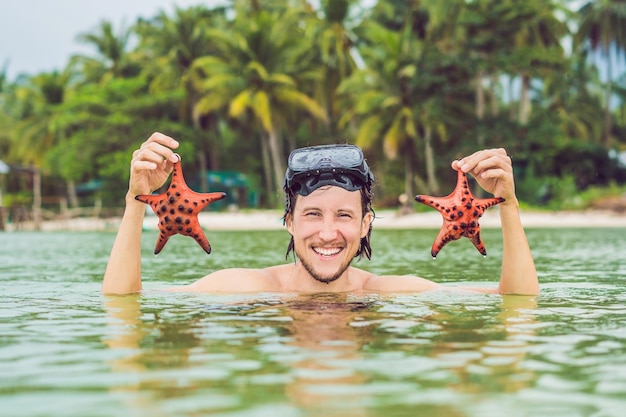 Feliz joven buzo sosteniendo una estrella de mar sonriendo mirando a la cámara