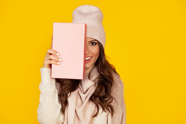 Feliz joven con una caja de regalo en sus manos, cubre la mitad de su rostro con un regalo de año nuevo.